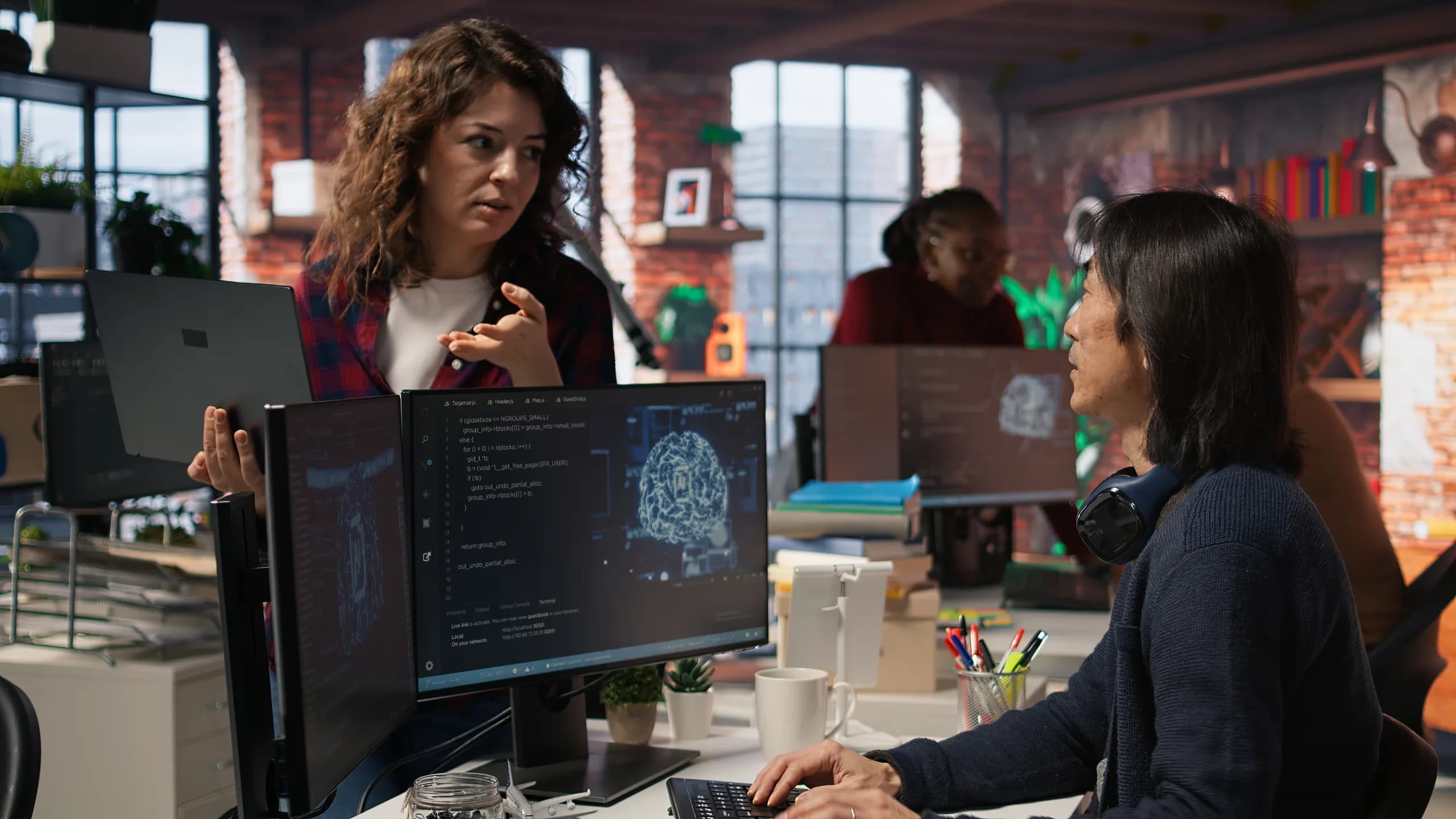 A young team member holding a laptop and asking a senior technician a question in a startup workspace
