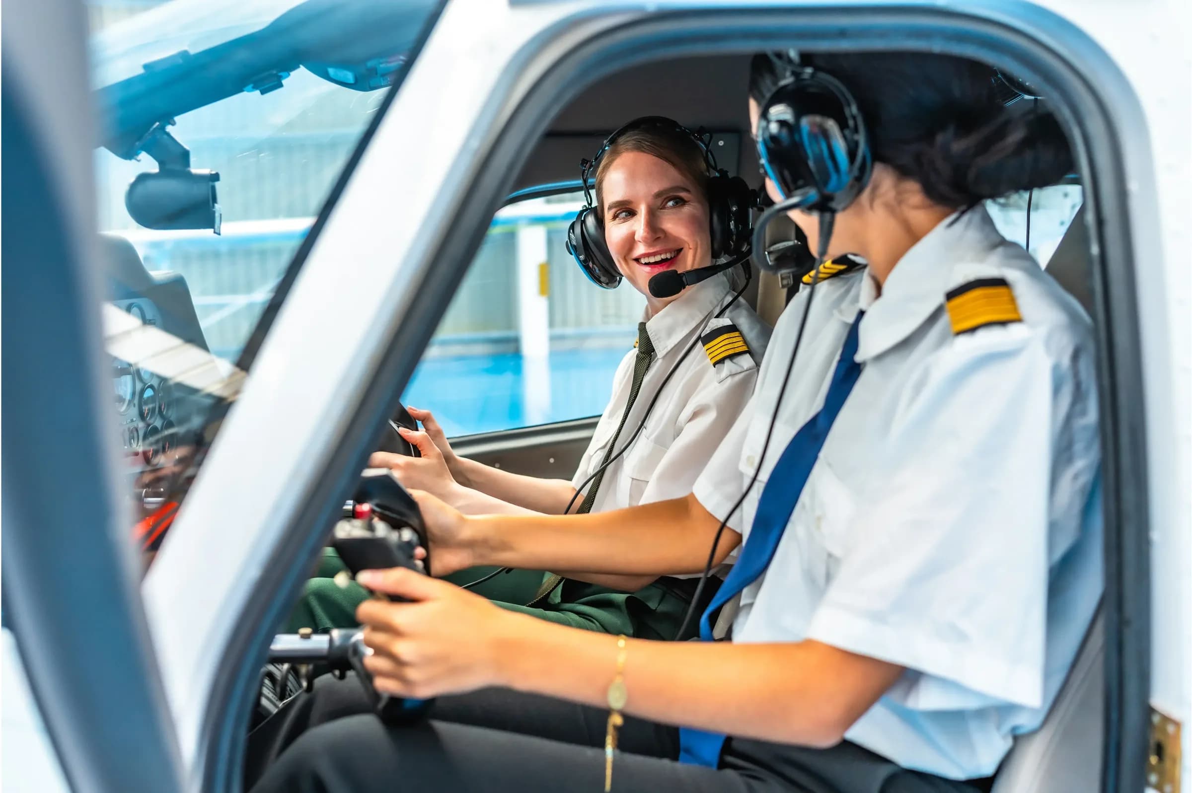 A flight instructor and a trainee pilot in headsets at the controls of a light aircraft, seen through the open cockpit door