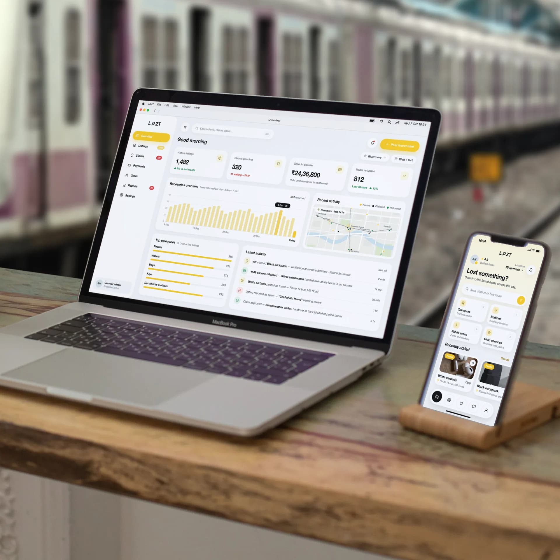 The Loztapp platform we built, on a MacBook Pro and an iPhone in a stand on a desk on a railway platform: the operator overview with 1,482 active listings, 320 claims pending and ₹24,36,800 held in escrow, and the app's “Lost something?” home on the phone