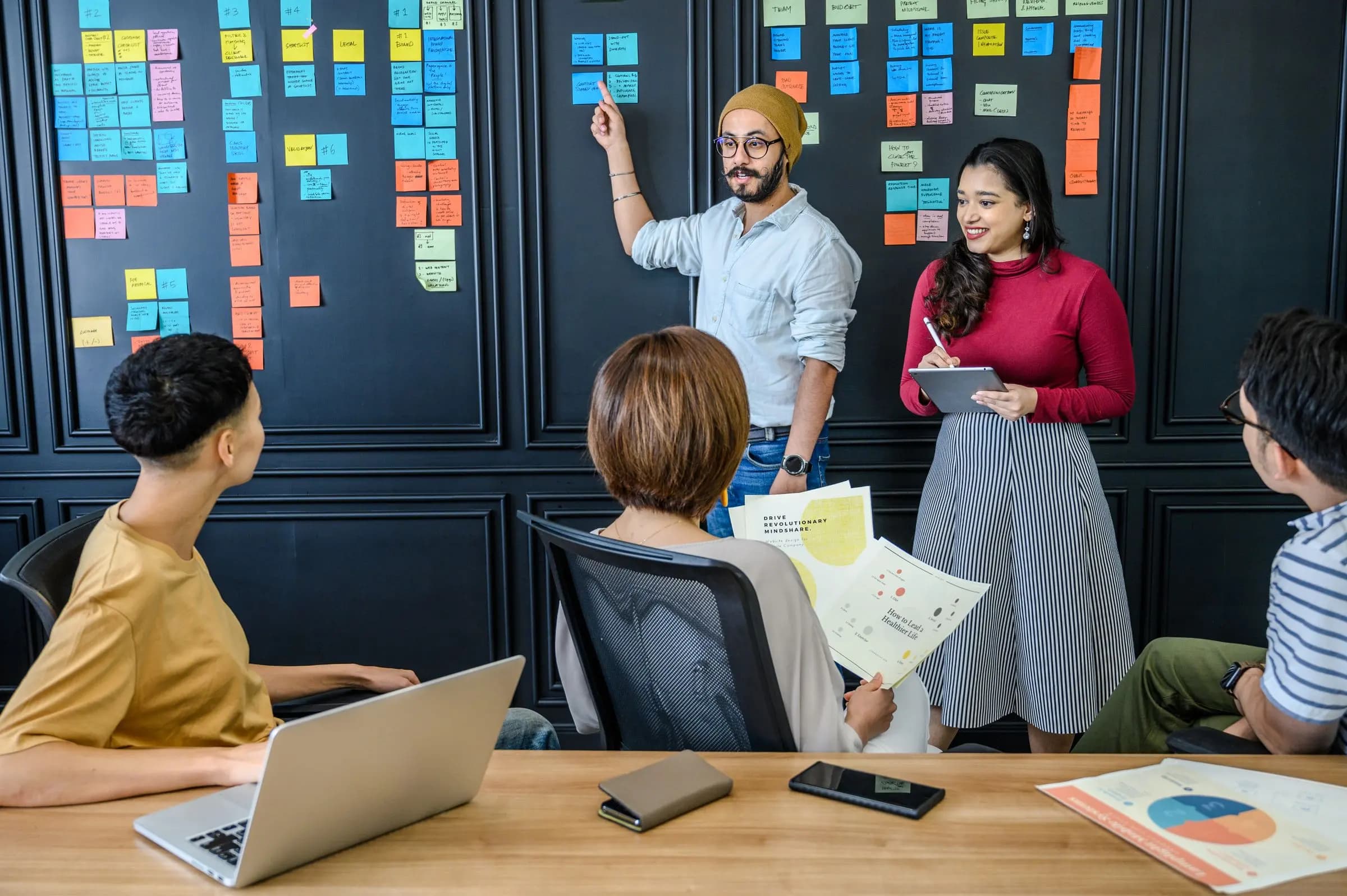 A team meets in front of a wall of colour-coded sticky notes as one member points to a card.