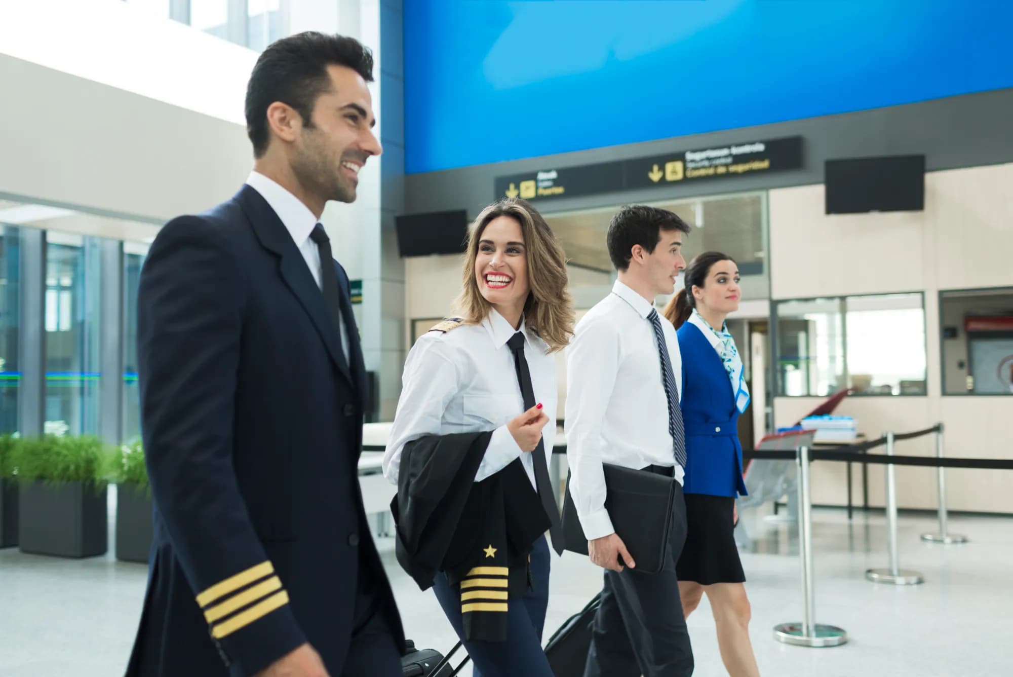 An airline captain, two pilots in white uniform shirts and a cabin crew member walking through an airport terminal