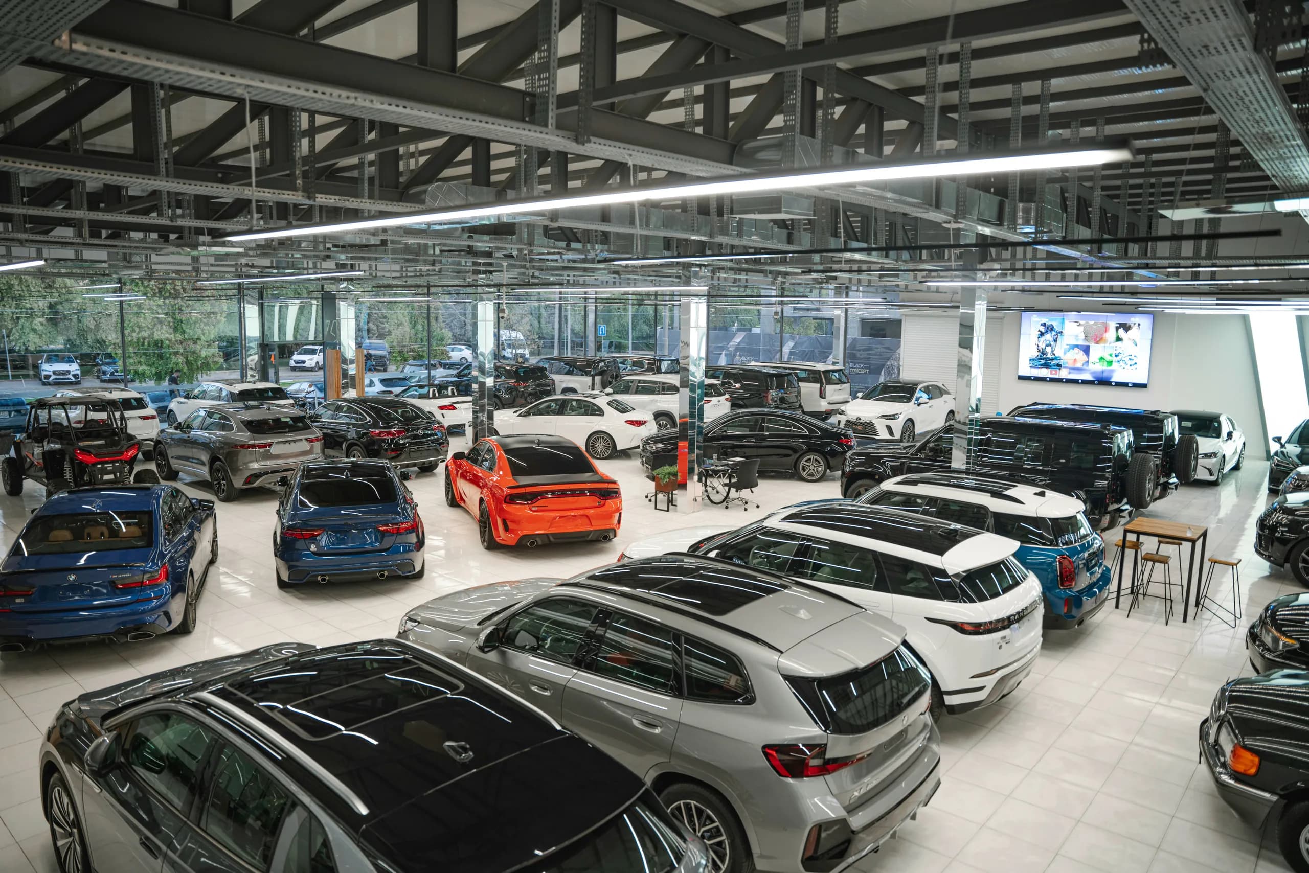 Rows of new cars and SUVs on a bright showroom floor under exposed steel roof trusses