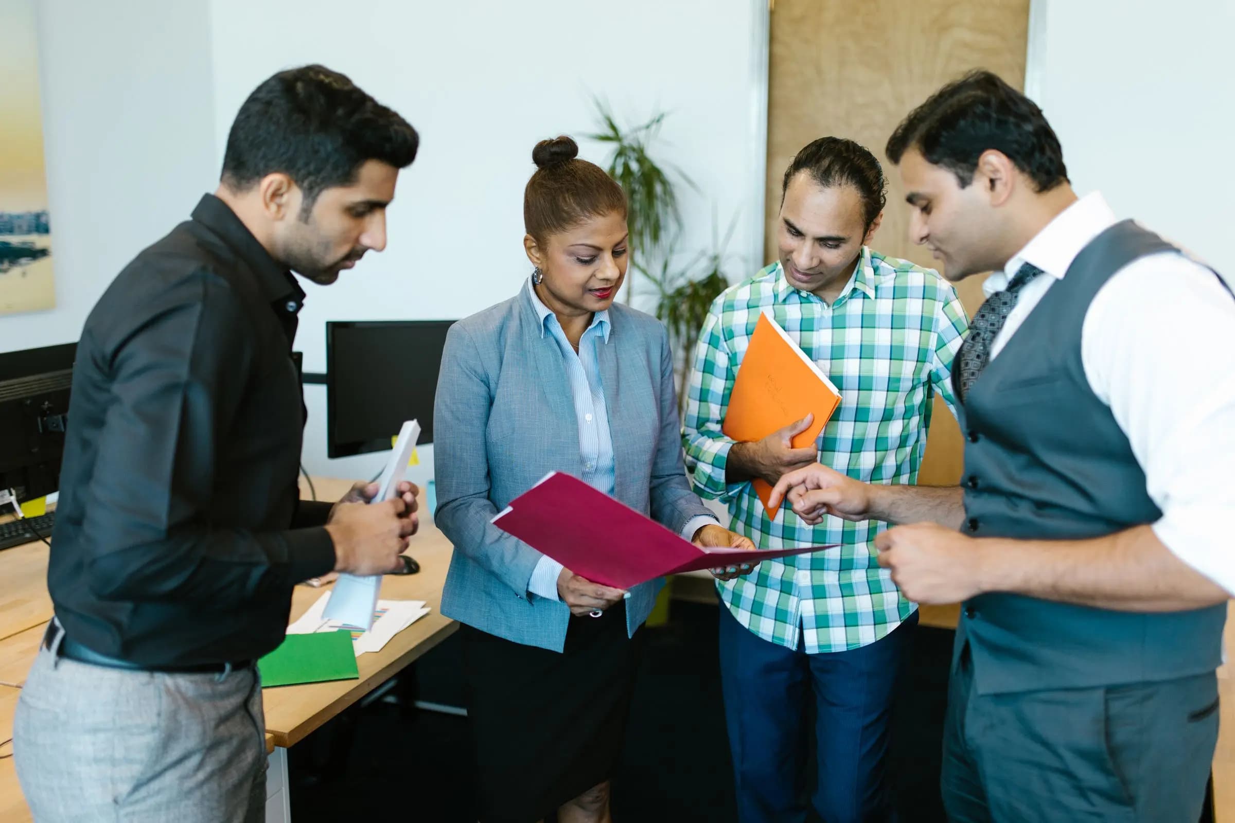 Four colleagues gather around an open folder, pointing at the pages as they discuss them.