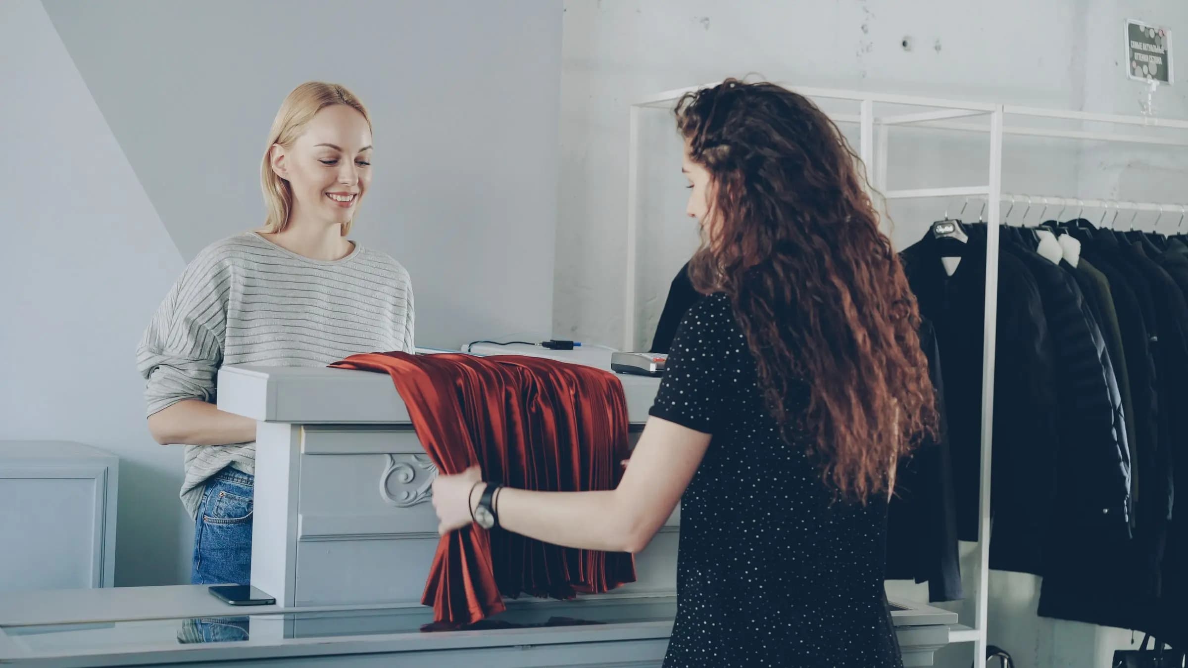 A shop assistant smiles at a customer laying a garment on the counter of a clothing store.