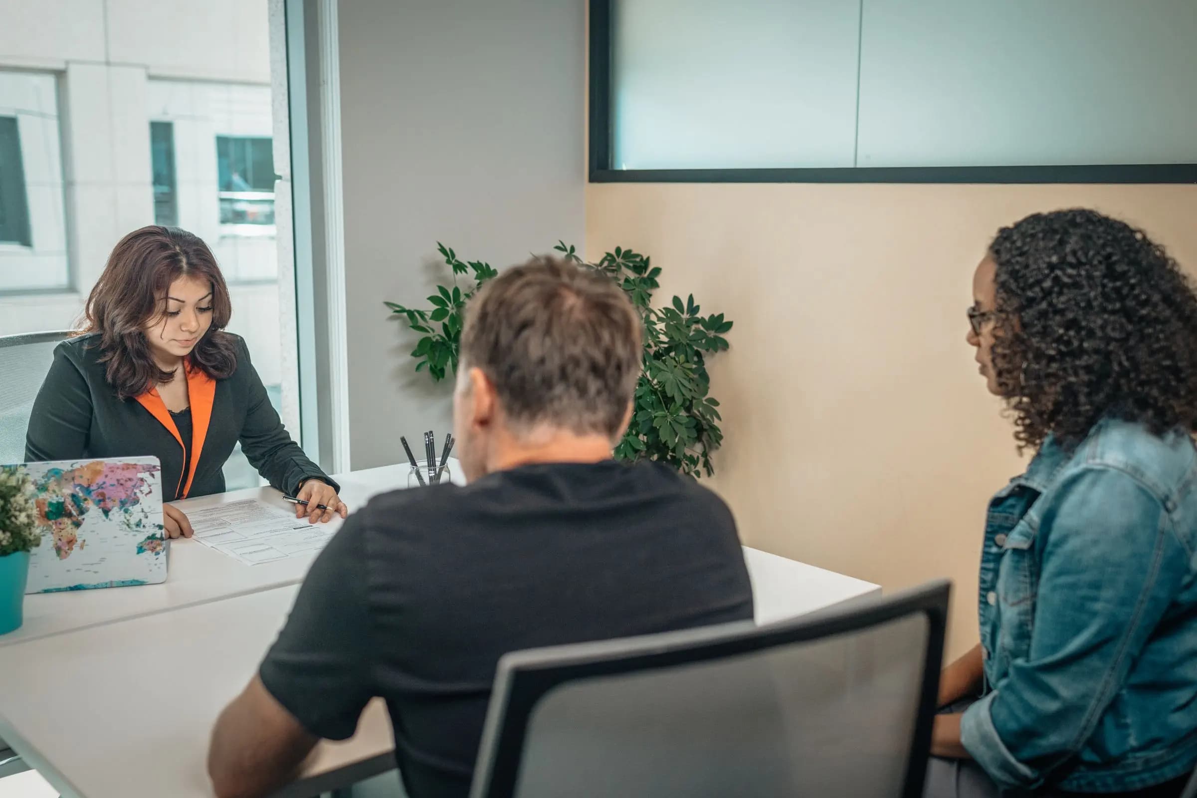 A woman at a desk goes over a document with two clients seated across from her.
